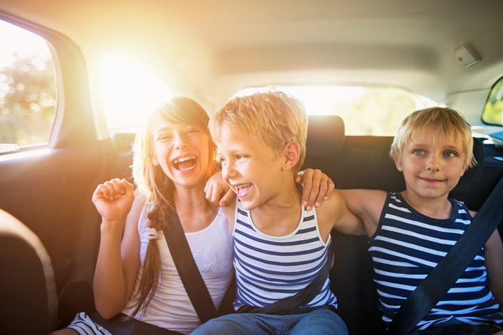 Three kids laughing in car on a road trip. Kids are aged 10 and 7. The kids are laughing and embracing, Sunny summer day.